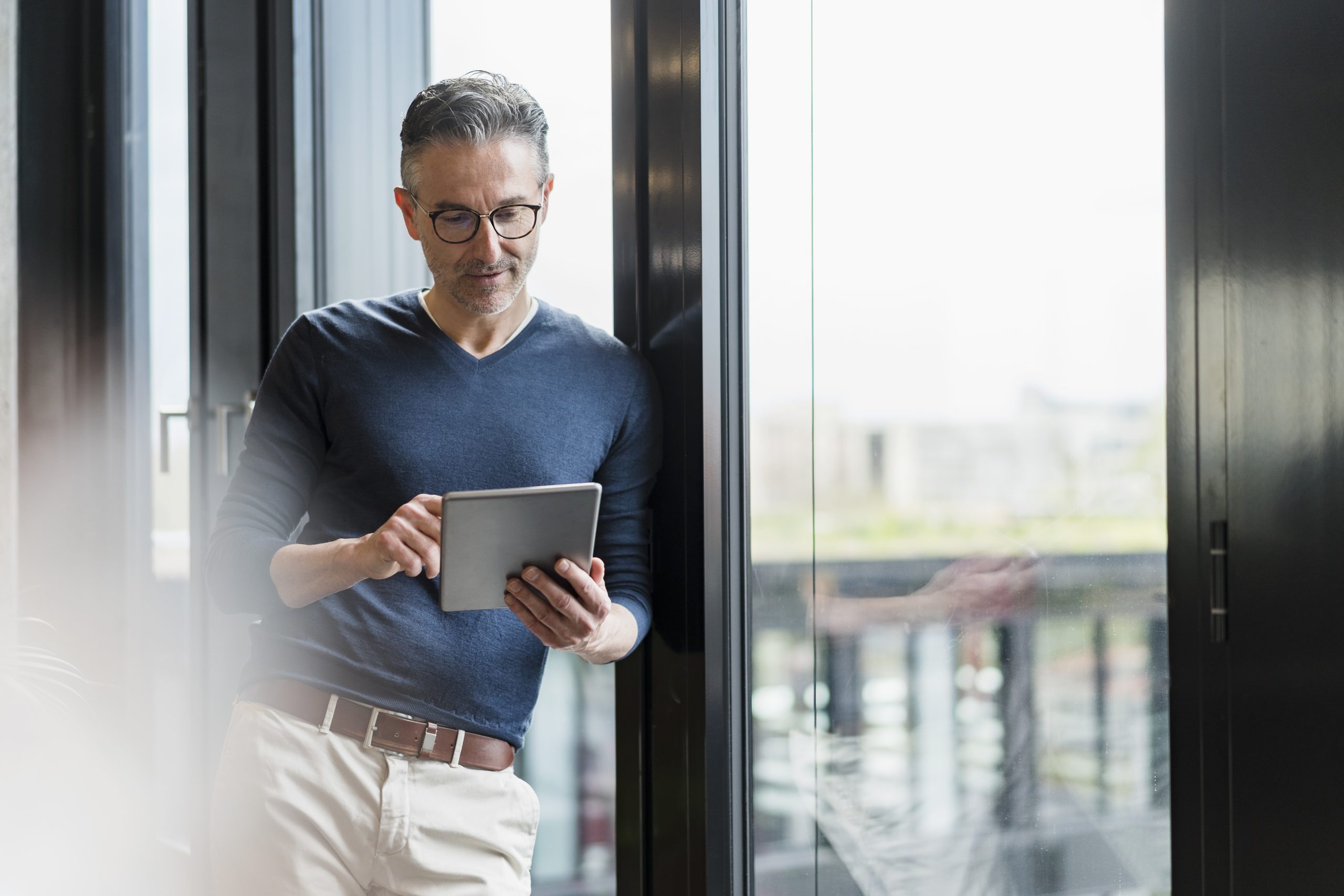Male entrepreneur using digital tablet while leaning on glass window in office